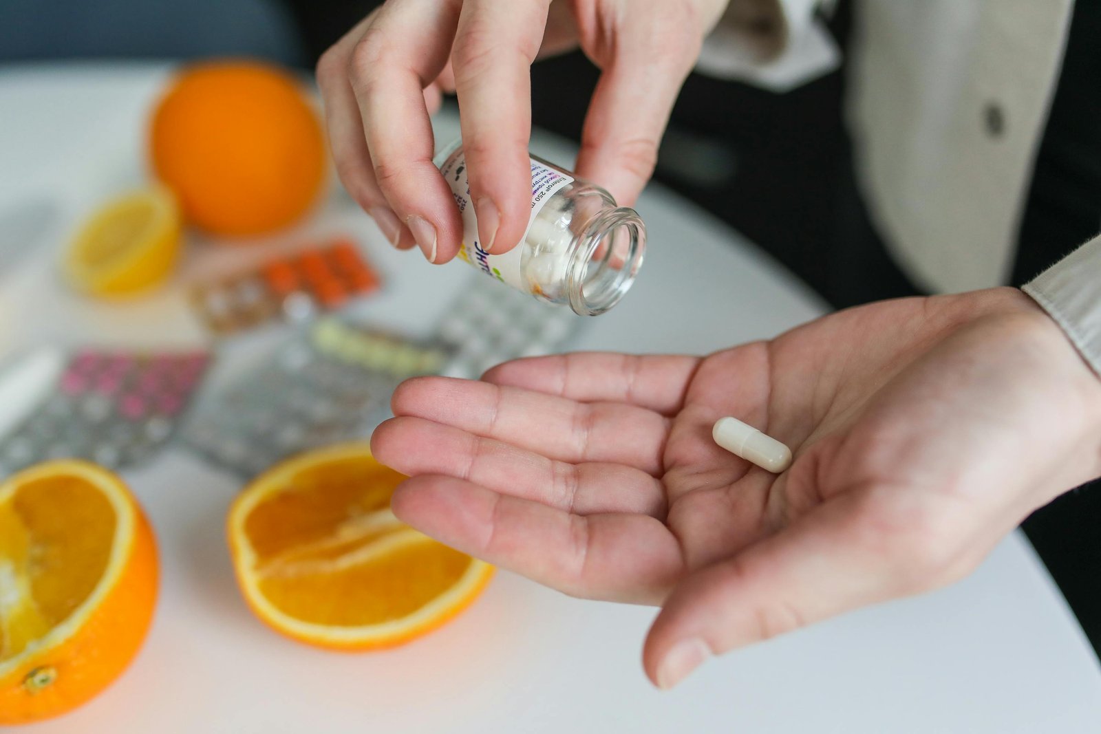 A capsule being poured from a bottle into an open hand beside fresh oranges