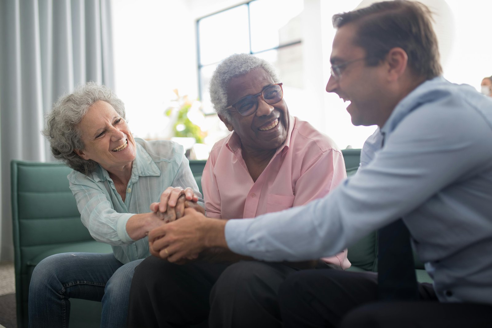 A caregiver holding hands and laughing with an elderly couple at home
