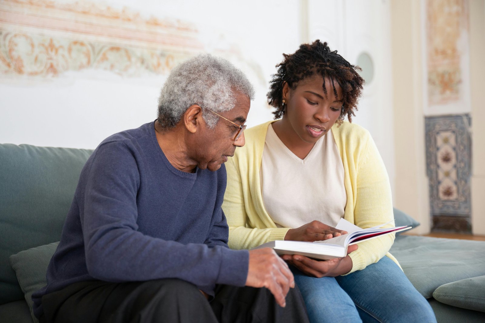 A MERICARE caregiver reading with an elderly man on the sofa at home